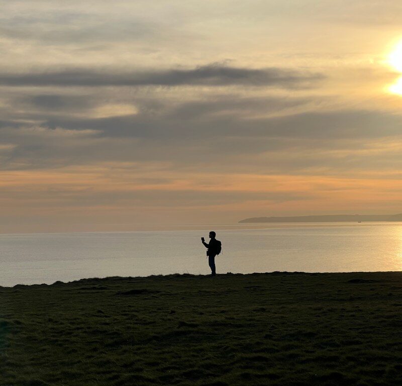 Silhouette of a person walking along a coastline at sunset